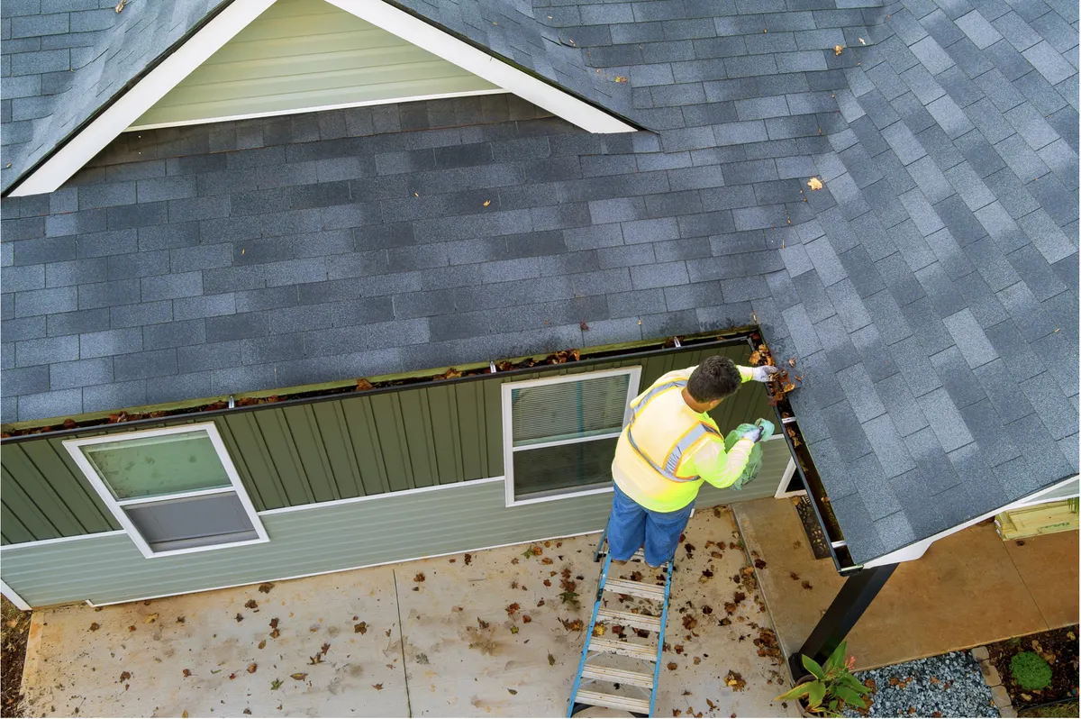 Professional clearing leaves from gutters on a ladder at a single-family home